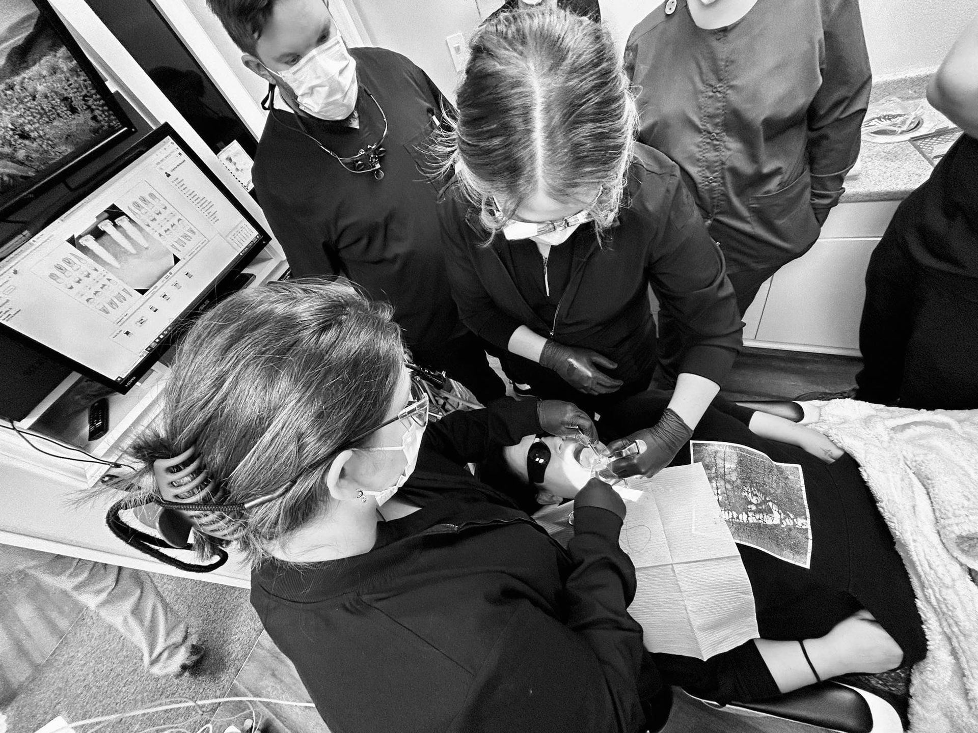 Dentists examining patient's teeth, surrounded by colleagues. Inside a dental clinic. Black and white.