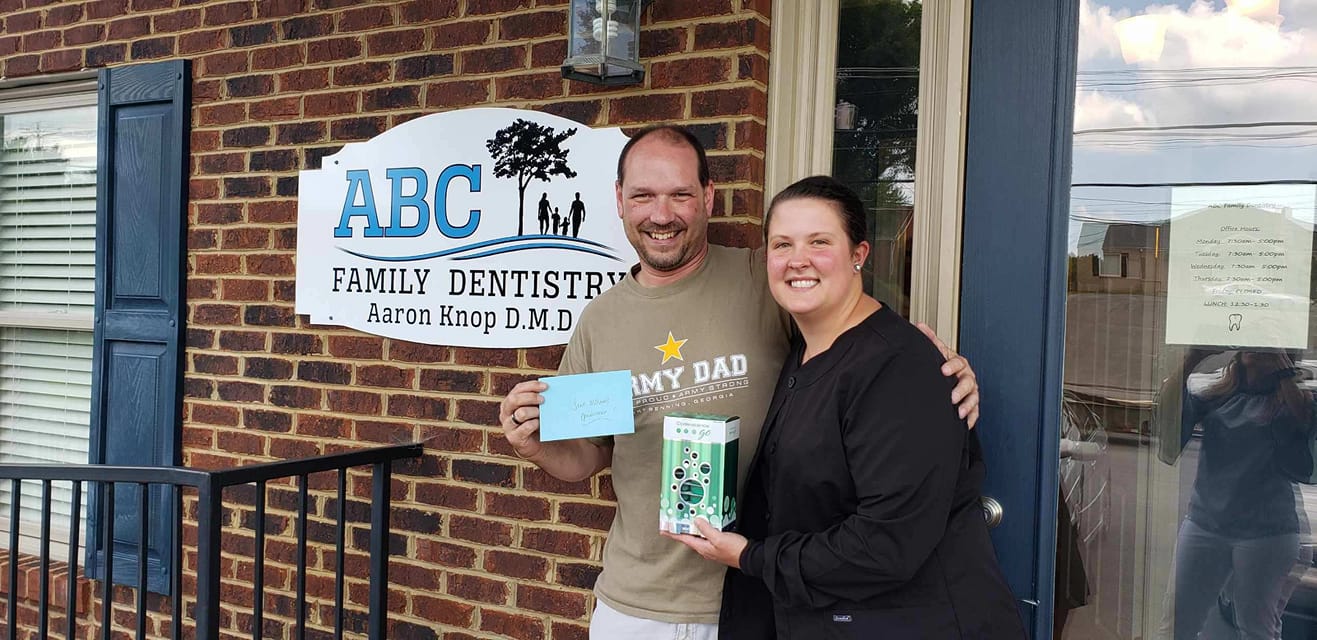 Two people outside a brick building. One holds a blue paper, the other holds a gift box. They smile.