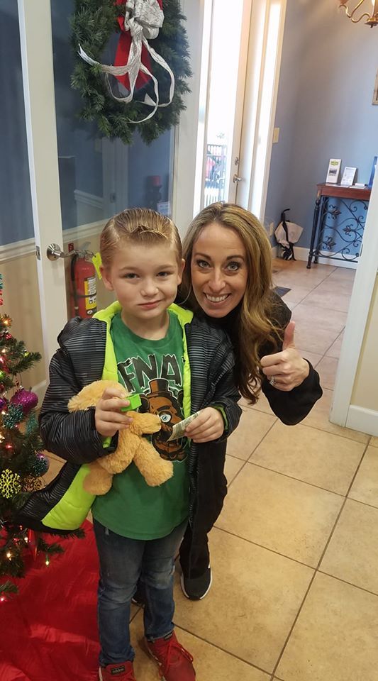 A young boy and woman smile, pose by a Christmas tree. The woman gives a thumbs-up.