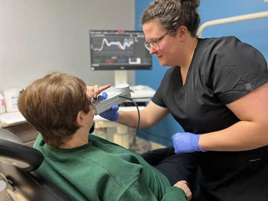 A dentist examining a patient's mouth with a handheld device in a dental office.