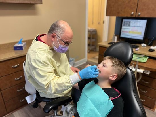 Dentist in mask and gloves examines a child's teeth in a dental office.