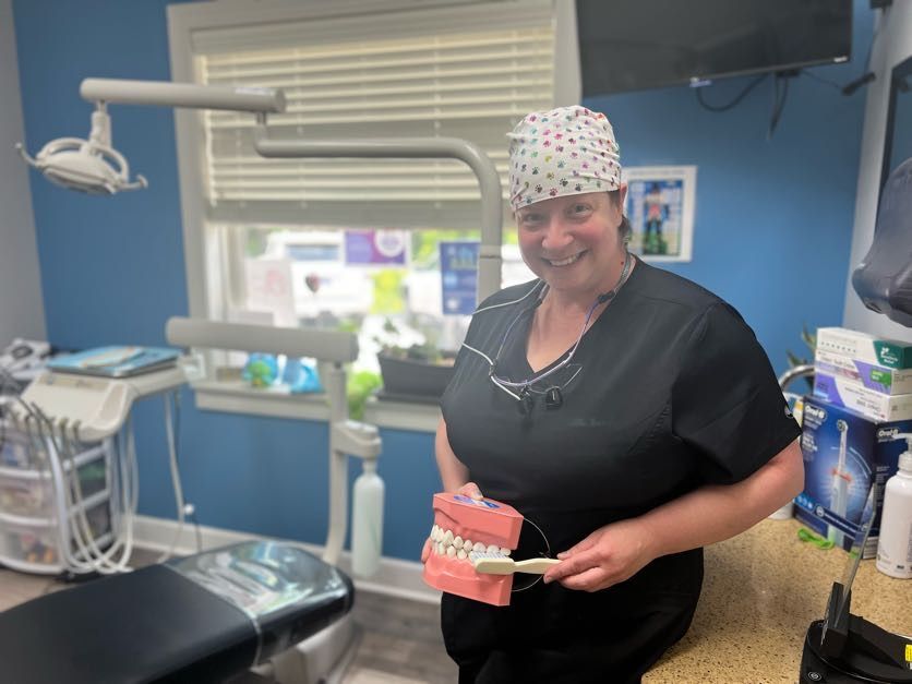 Dentist in a dental office holding a teeth model and toothbrush, smiling.