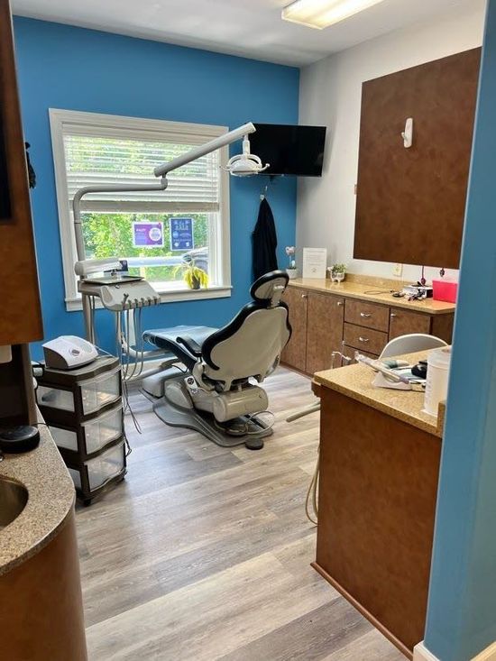 Dental office interior with blue walls, dental chair, equipment, and a window.
