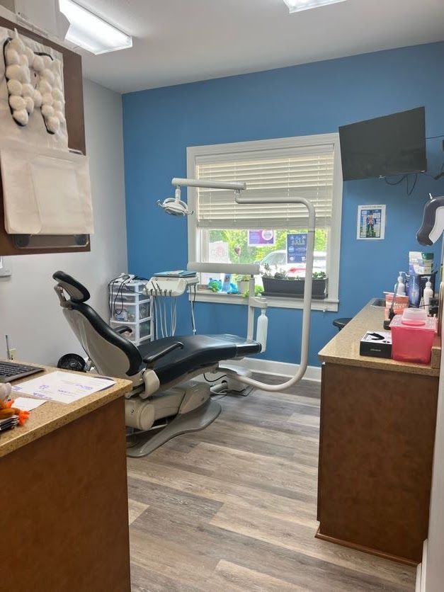 Dental operatory with chair, blue walls, window, and equipment.