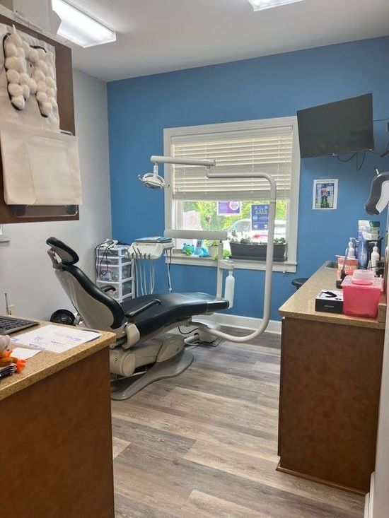 Dental operatory with chair, blue walls, window, and equipment.