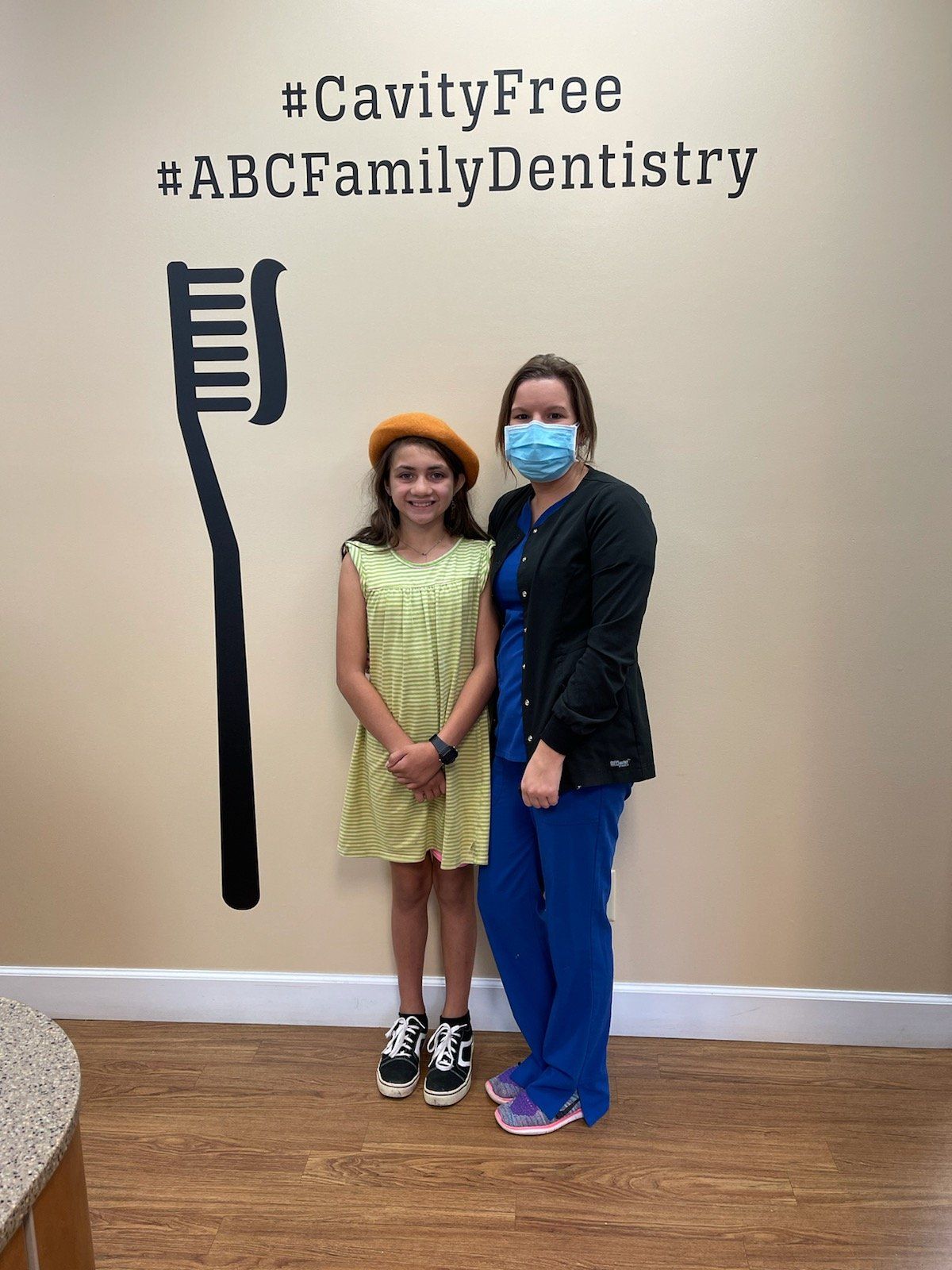 Girl and dentist posing in front of a dental clinic wall with a toothbrush design and text.