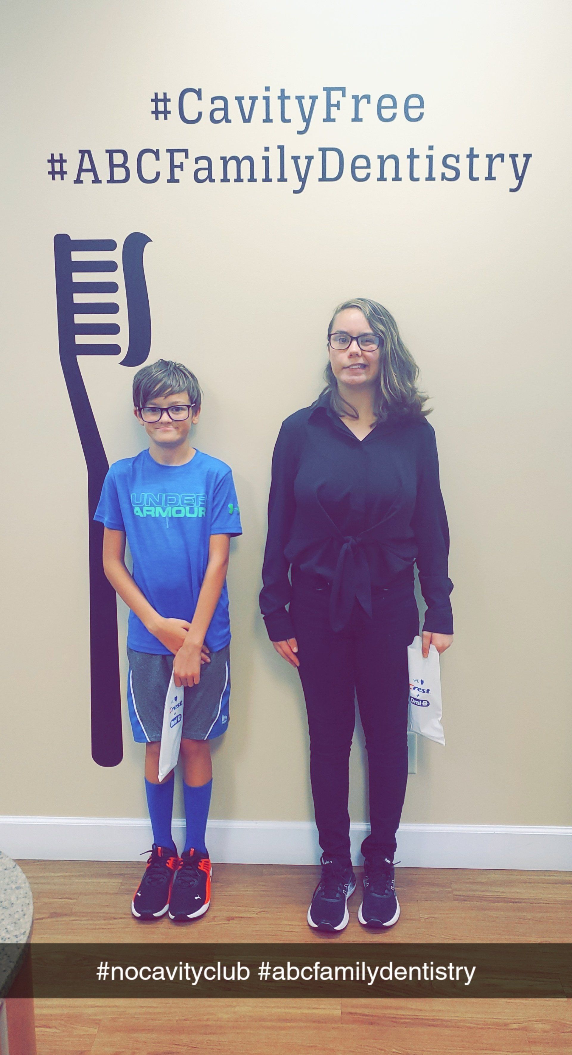 A boy and woman stand beside a toothbrush graphic and text at a dental office.