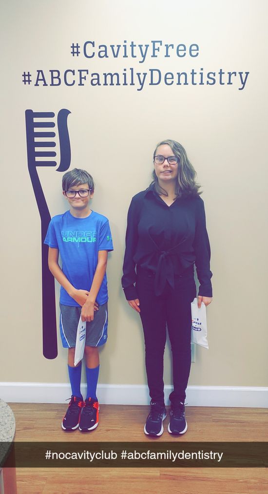 A boy and woman stand beside a toothbrush graphic and text at a dental office.