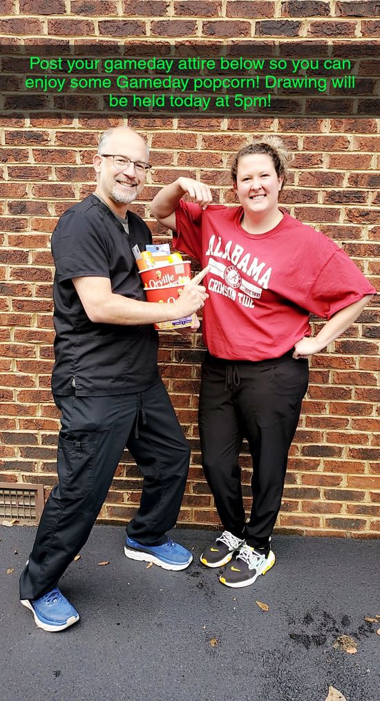 A man and woman pose by a brick wall. The man holds popcorn and the woman wears a red shirt with 