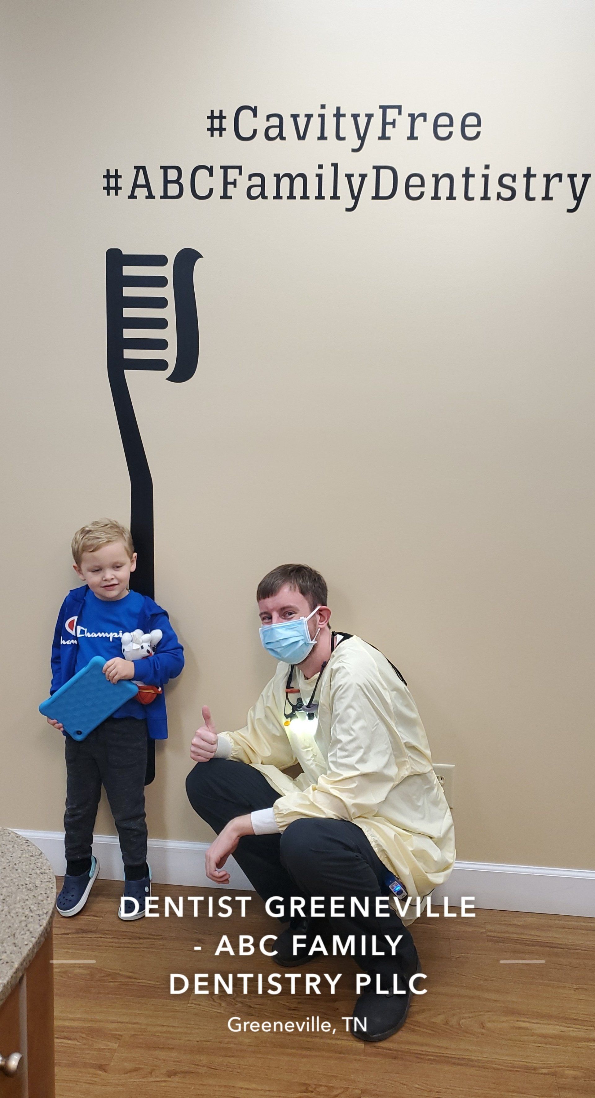 A dentist and young patient pose with a toothbrush graphic in a dental office.