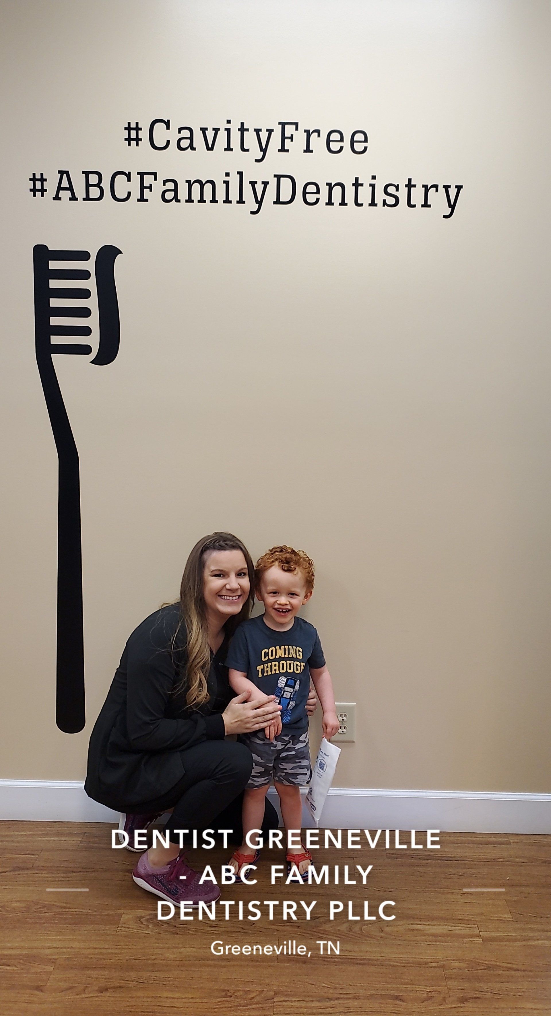 Woman and child pose in front of wall art, with text and a toothbrush cutout for a dental office.
