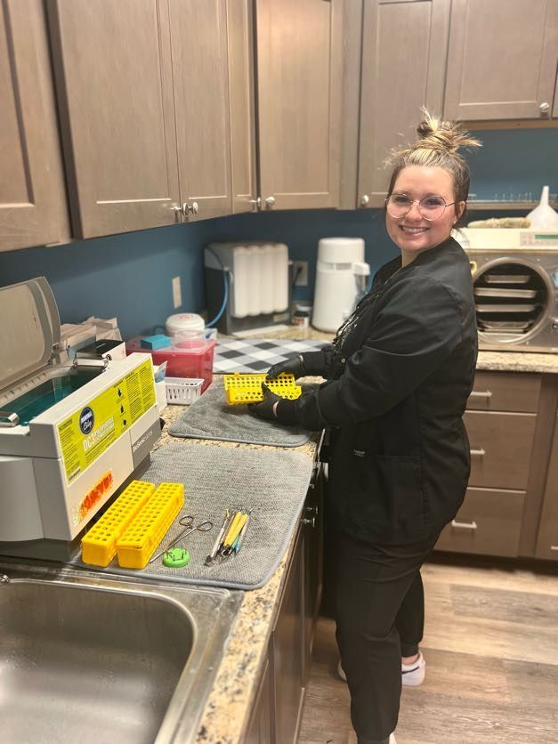 Woman in scrubs preparing dental tools; sterilization room.