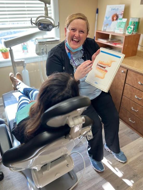 Dentist explains tooth diagram to patient in dental chair; bright room, smiling expressions.