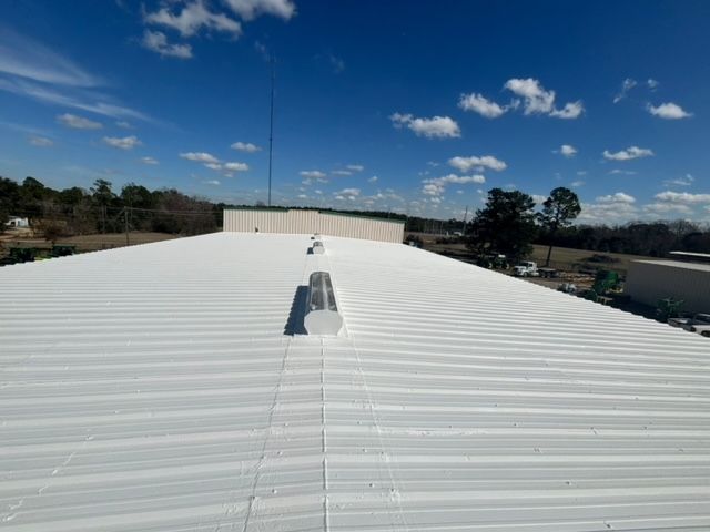 White commercial metal roof under a blue sky with scattered clouds.