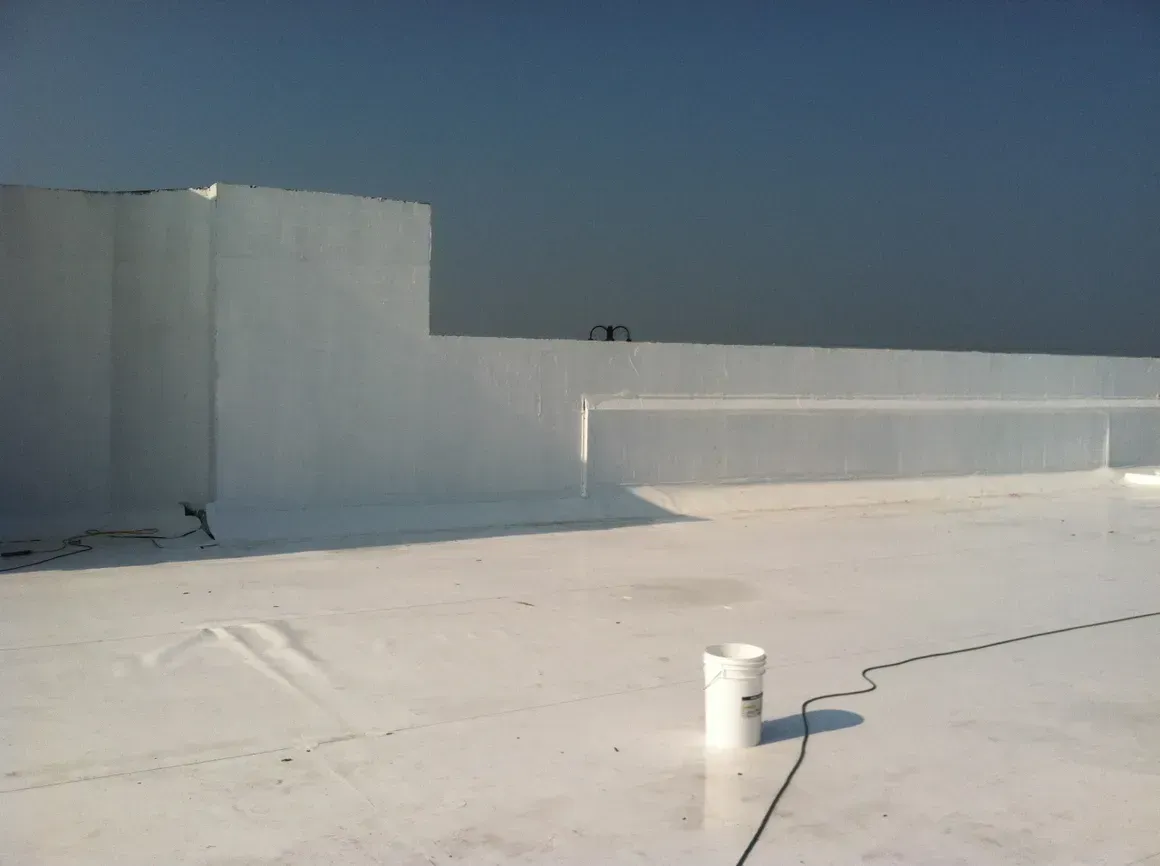 White painted roof and wall under a light blue sky. A bucket and cable are on the roof.