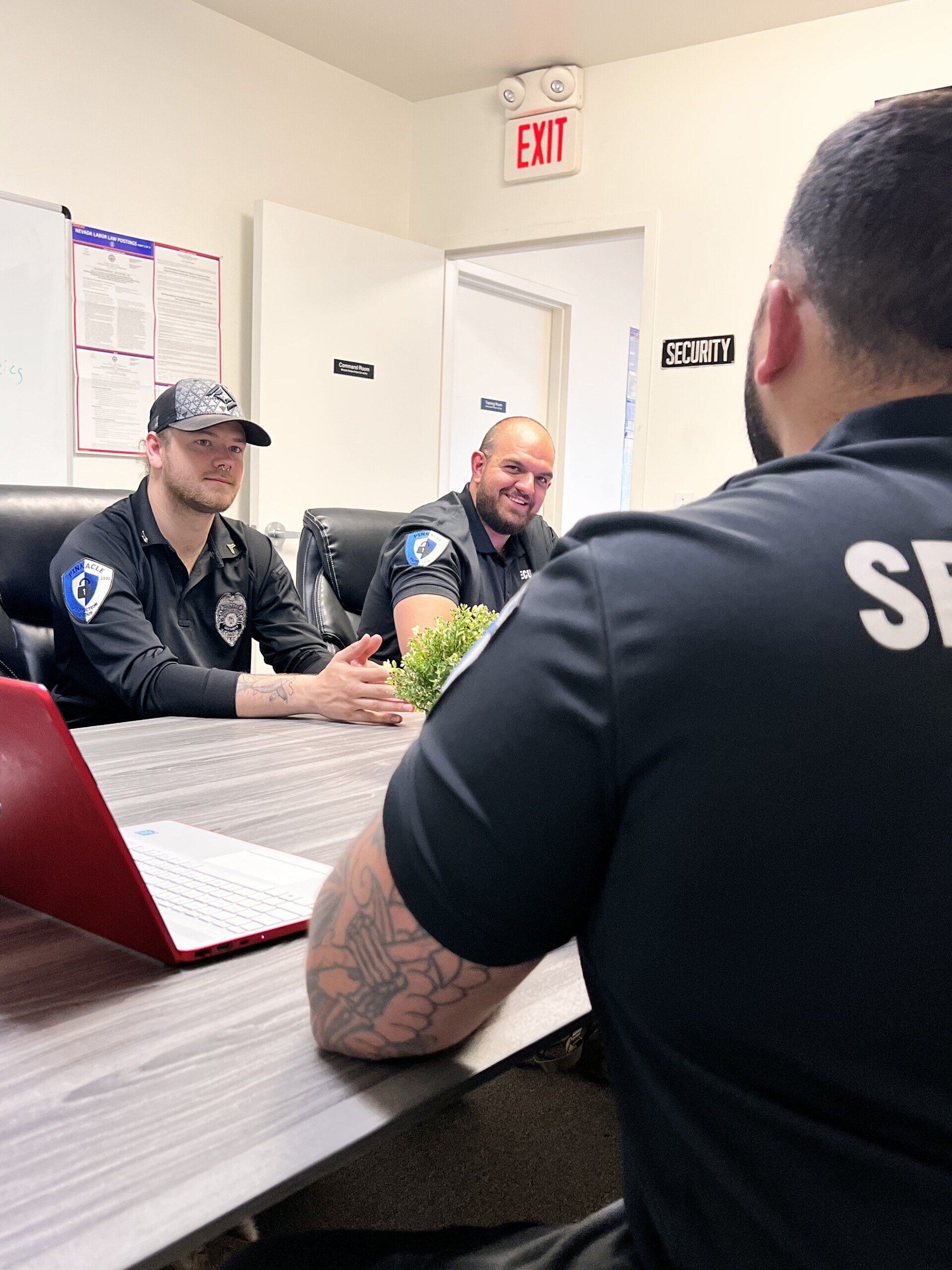 a group of security officers are sitting at a table with a laptop .