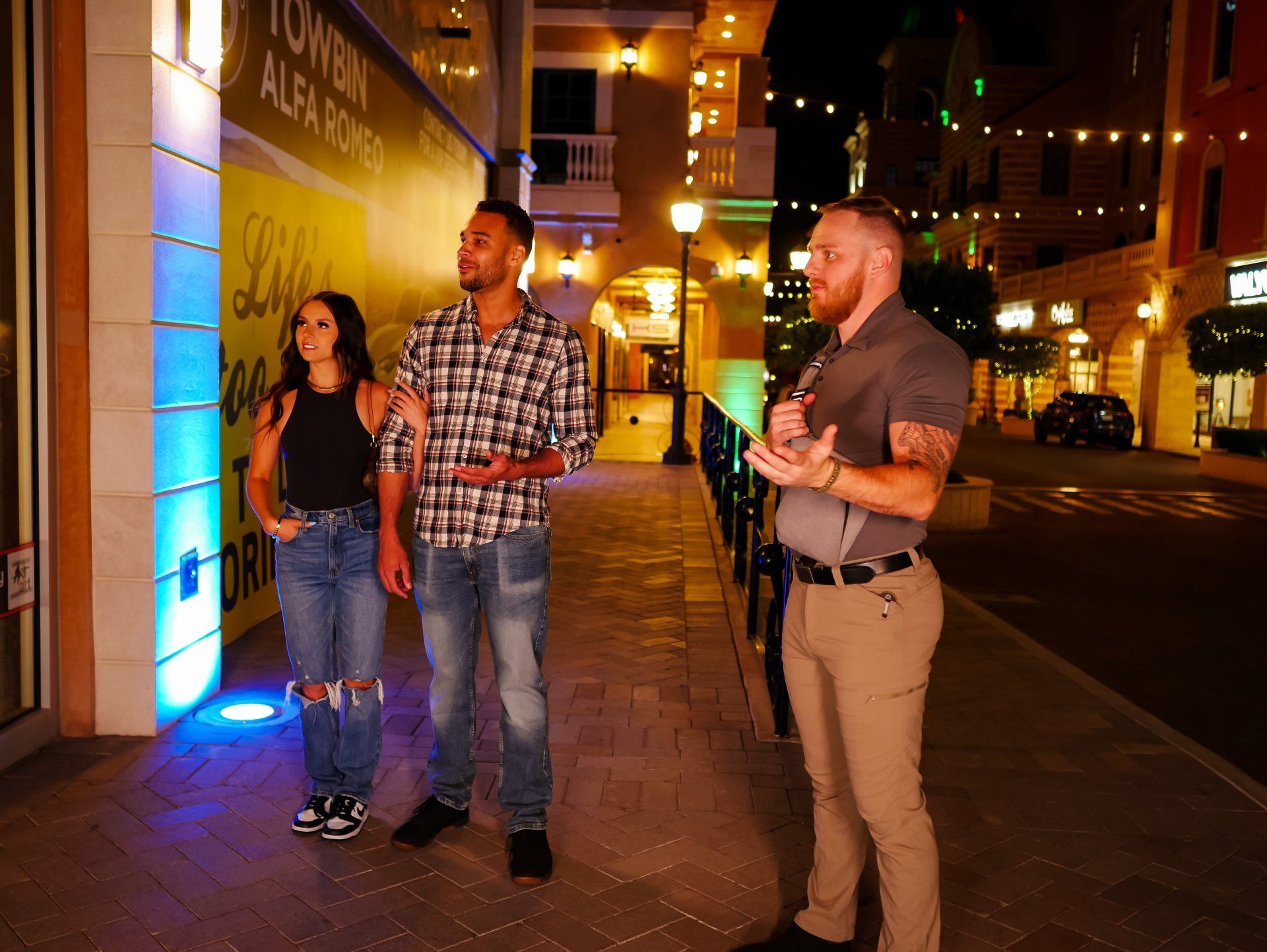 Two men and a woman are walking down a sidewalk at night.