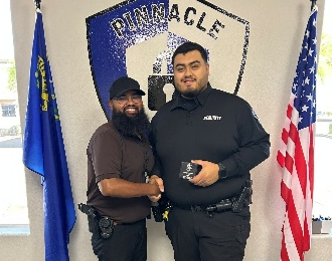 Two men in uniform shaking hands in front of flags and a police badge.