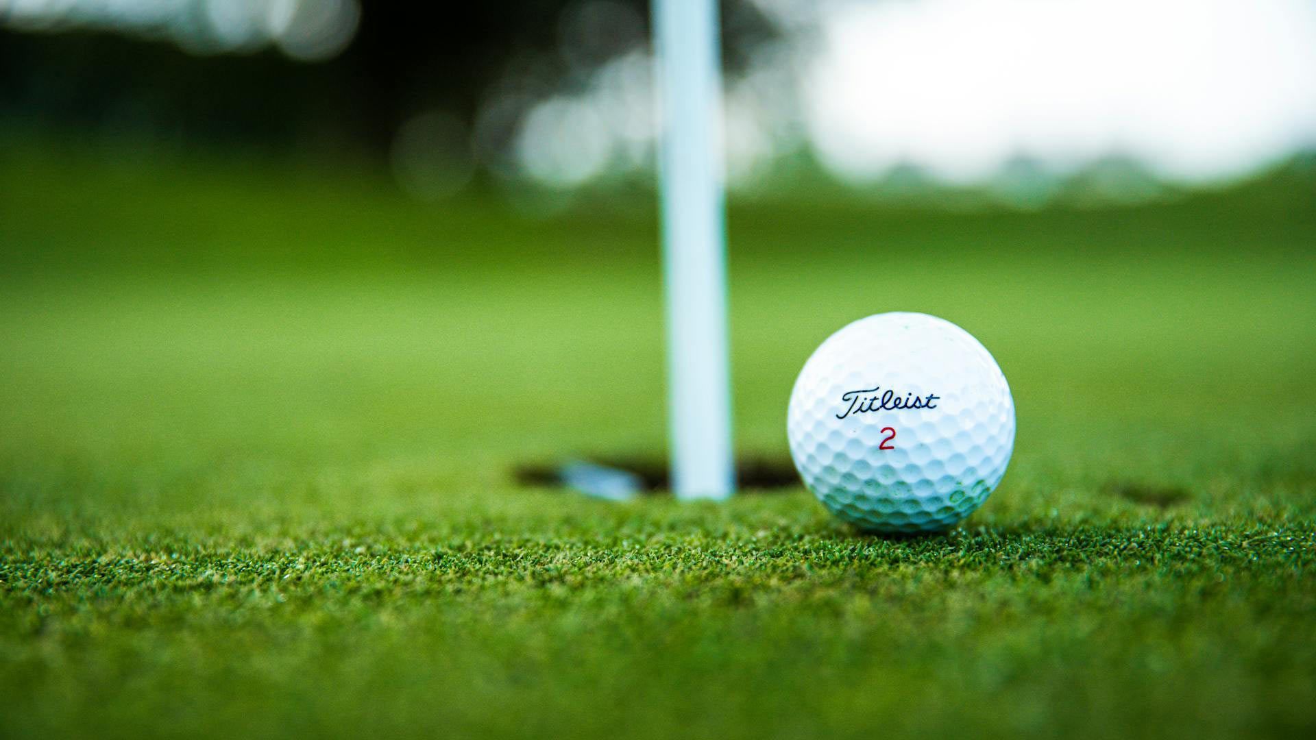 Golf ball near the hole on a green, with a white flag in the background.