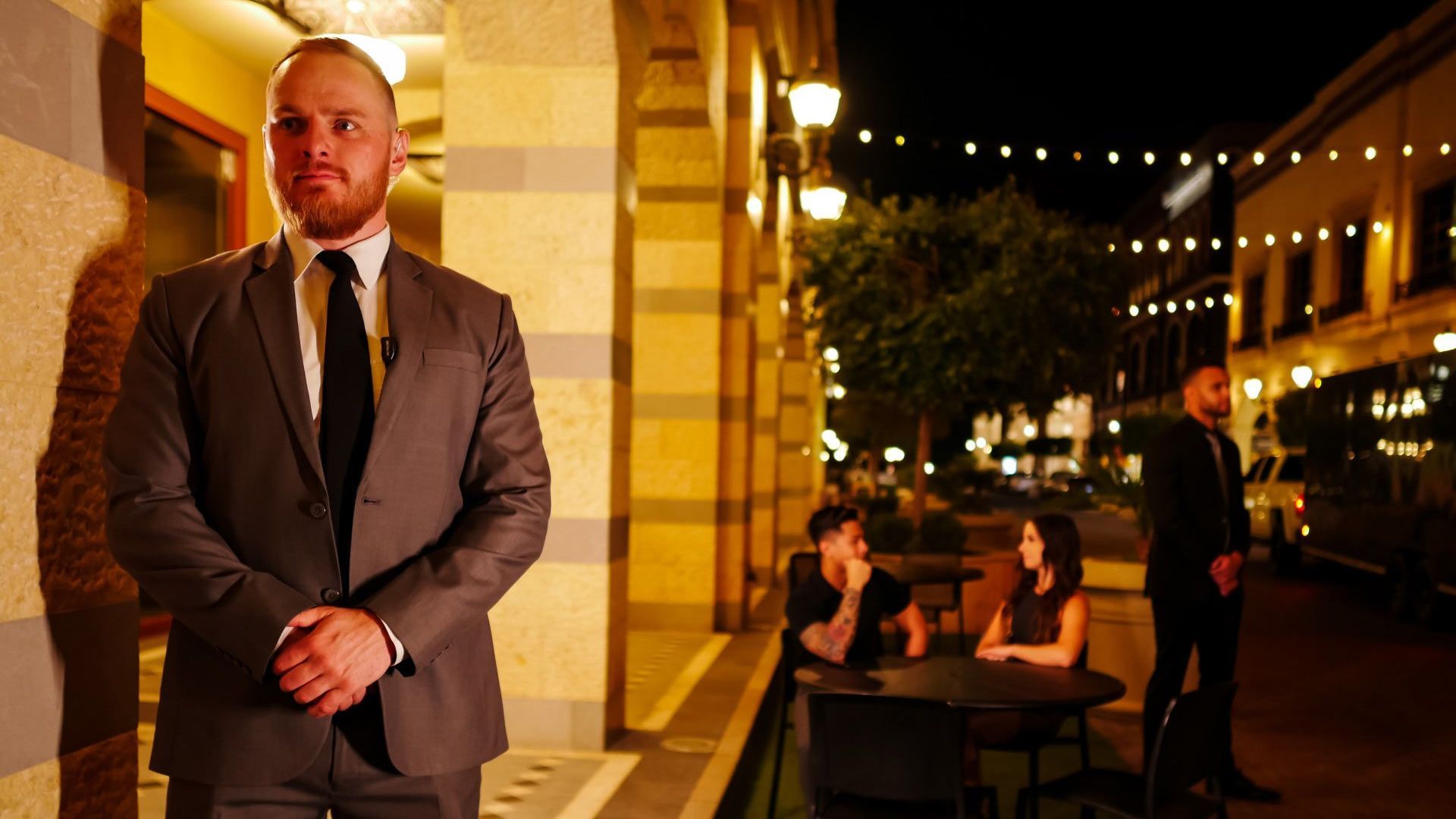 A man in a suit and tie is standing in front of a group of people sitting at tables.