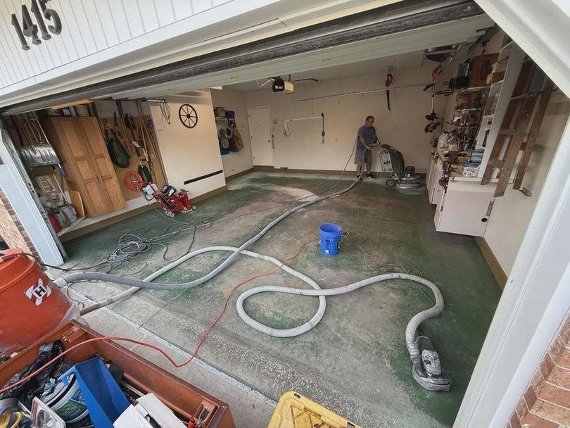 Garage floor being pressure-washed, with hoses, cleaning equipment, and a worker in the back.