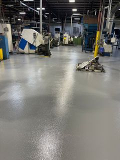 Industrial workshop with a wet floor reflecting overhead lights and machinery in the background