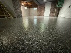 Basement with glossy speckled epoxy floor, exposed brick walls, and staircase in the corner