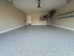 Empty garage with speckled floor, beige walls, white door, and shelves with stored items.