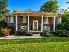 Brick house with white columns, front porch, and landscaped yard in bright sunlight
