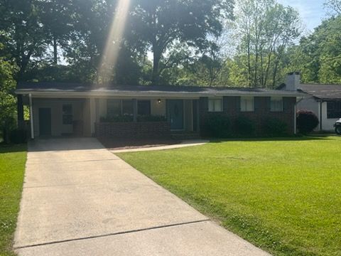 Single-story brick house with a long driveway and green front lawn in bright sunlight