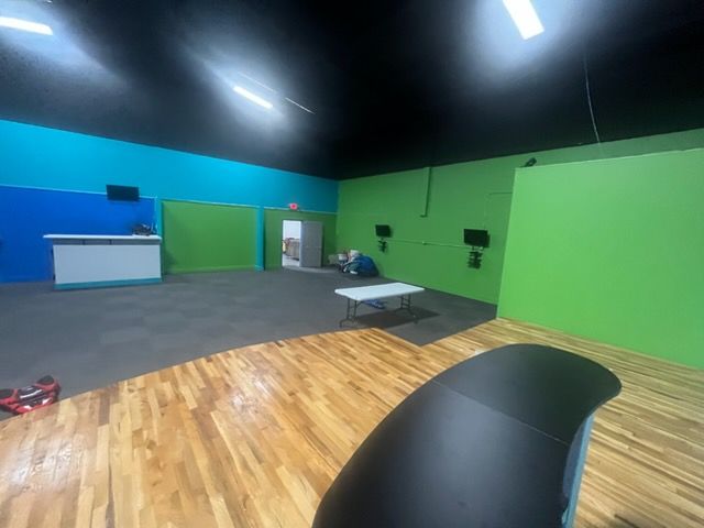 Empty indoor studio with green and blue walls, gray floor, bright ceiling lights, and a wooden platform in front.