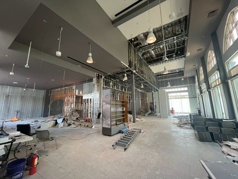 Large unfinished interior with exposed ceiling, scaffolding, construction materials, and tall windows.