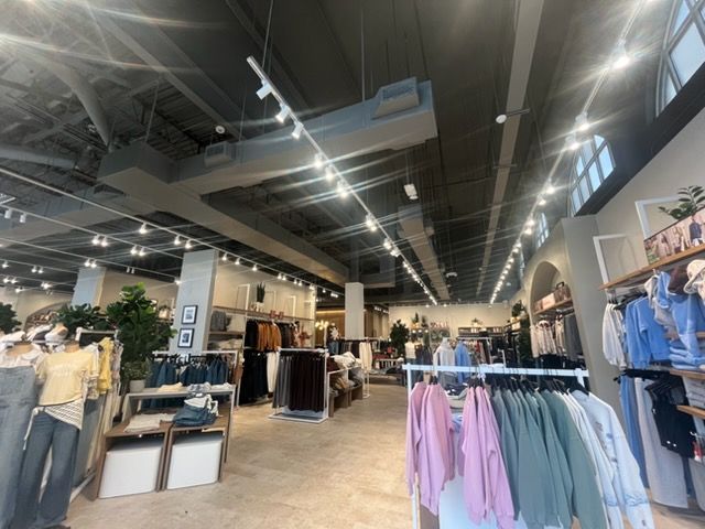 Clothing store interior with racks of shirts, dresses, and jackets under bright ceiling lights
