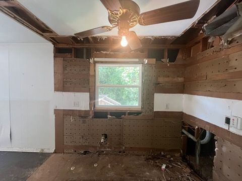 Partially demolished room with exposed walls, ceiling fan, window, and debris on the floor