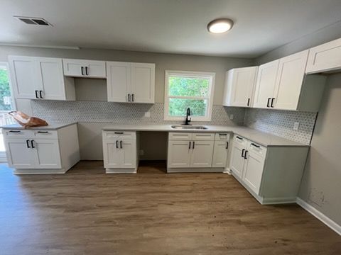 Modern white kitchen with gray backsplash, wood floors, and a window above the sink