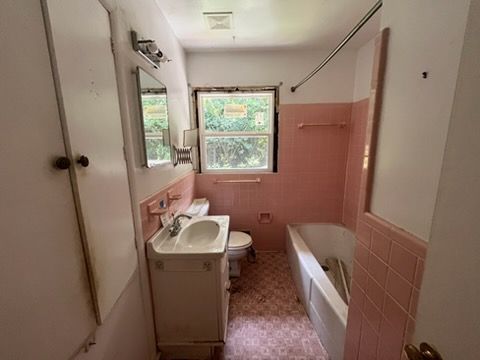 Small pink-tiled bathroom with sink, toilet, bathtub, and a window.