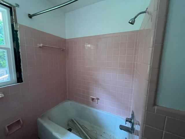 Pink-tiled bathroom with bathtub, wall-mounted shower head, and frosted glass window
