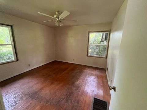 Empty room with hardwood floors, two windows, and a ceiling fan