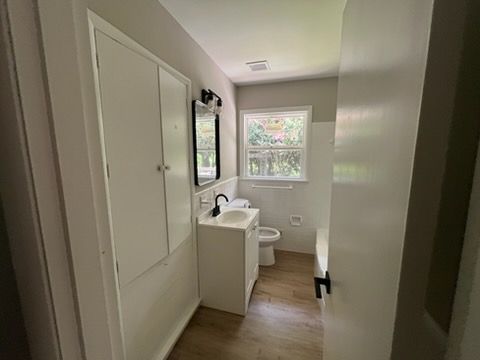 Narrow hallway leading to a small bathroom with white walls, mirror, sink, and window.