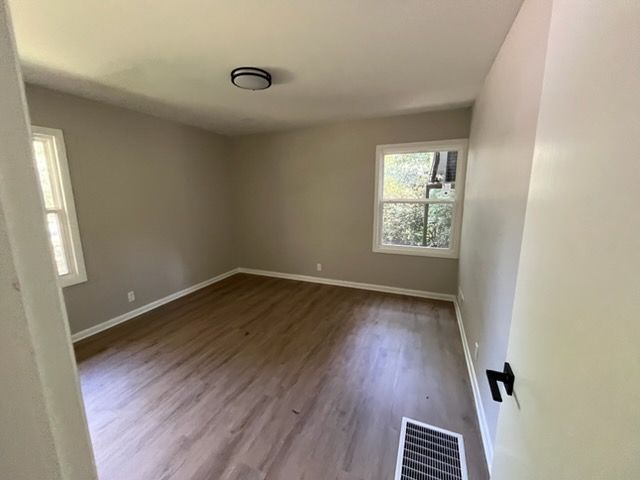 Empty beige room with wood flooring, two windows, and a ceiling light.