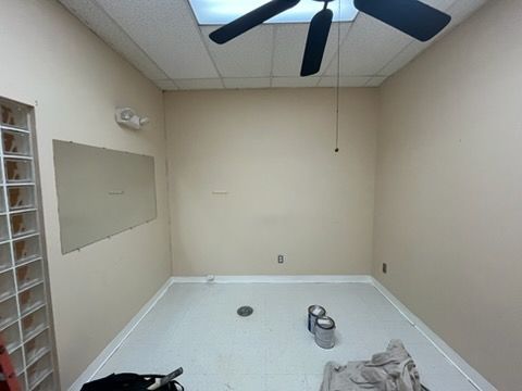 Empty beige room with ceiling fan, white floor, and a few items on the floor