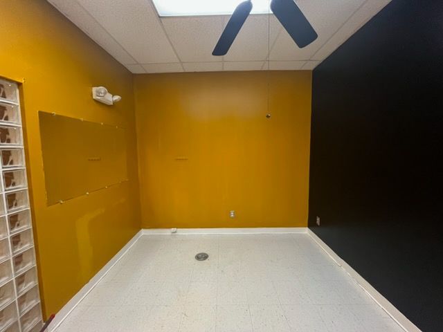 Empty room with mustard yellow walls, a black accent wall, white floor, and ceiling fan.