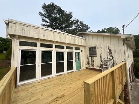 Wooden deck attached to a weathered white house with large sliding glass doors and a sloped roof.