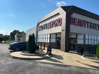Beauty & Beyond storefront with large signs, brick exterior, and parked car on a sunny day