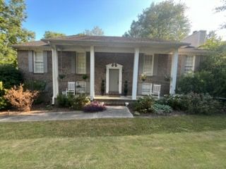 Single-story brick house with white columns, front porch, and a green lawn