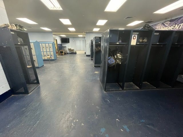 Empty locker room with black lockers, blue floor, and fluorescent ceiling lights