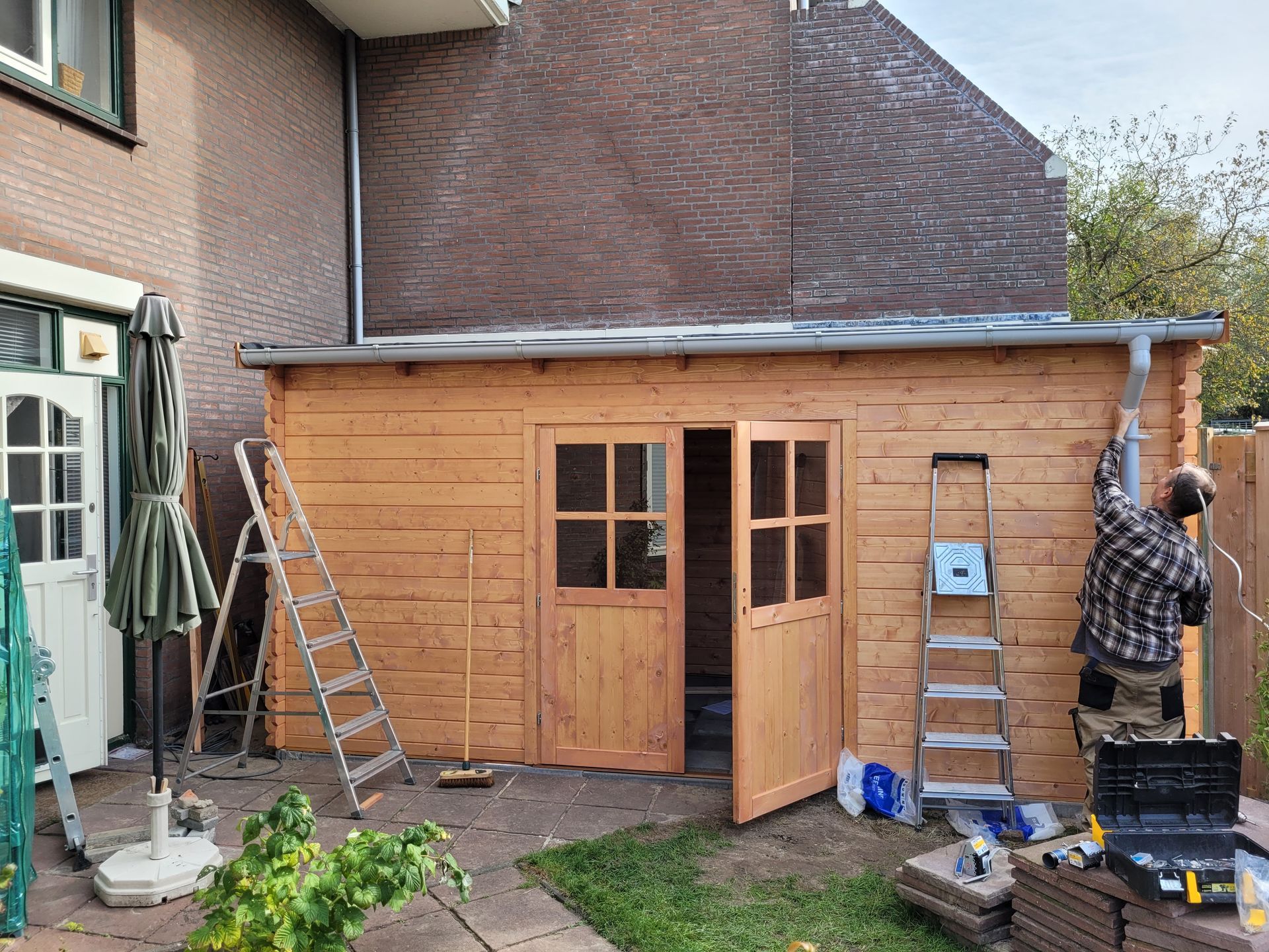 Iemand installeert een dakgoot op een nieuw gebouwde houten schuur in een achtertuin.