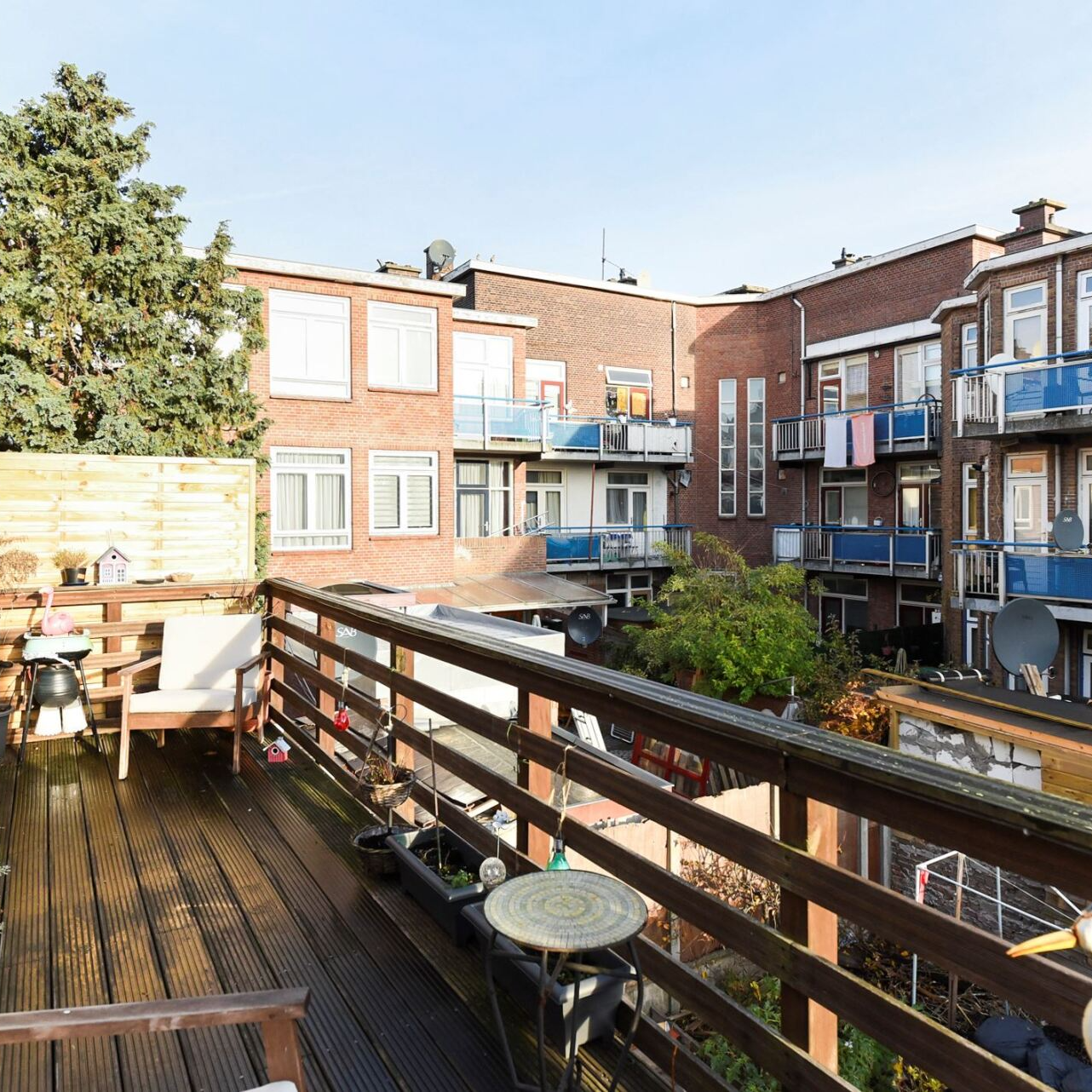 Een houten balkon met uitzicht op een binnenplaats, omgeven door bakstenen appartementencomplexen, op een zonnige dag.