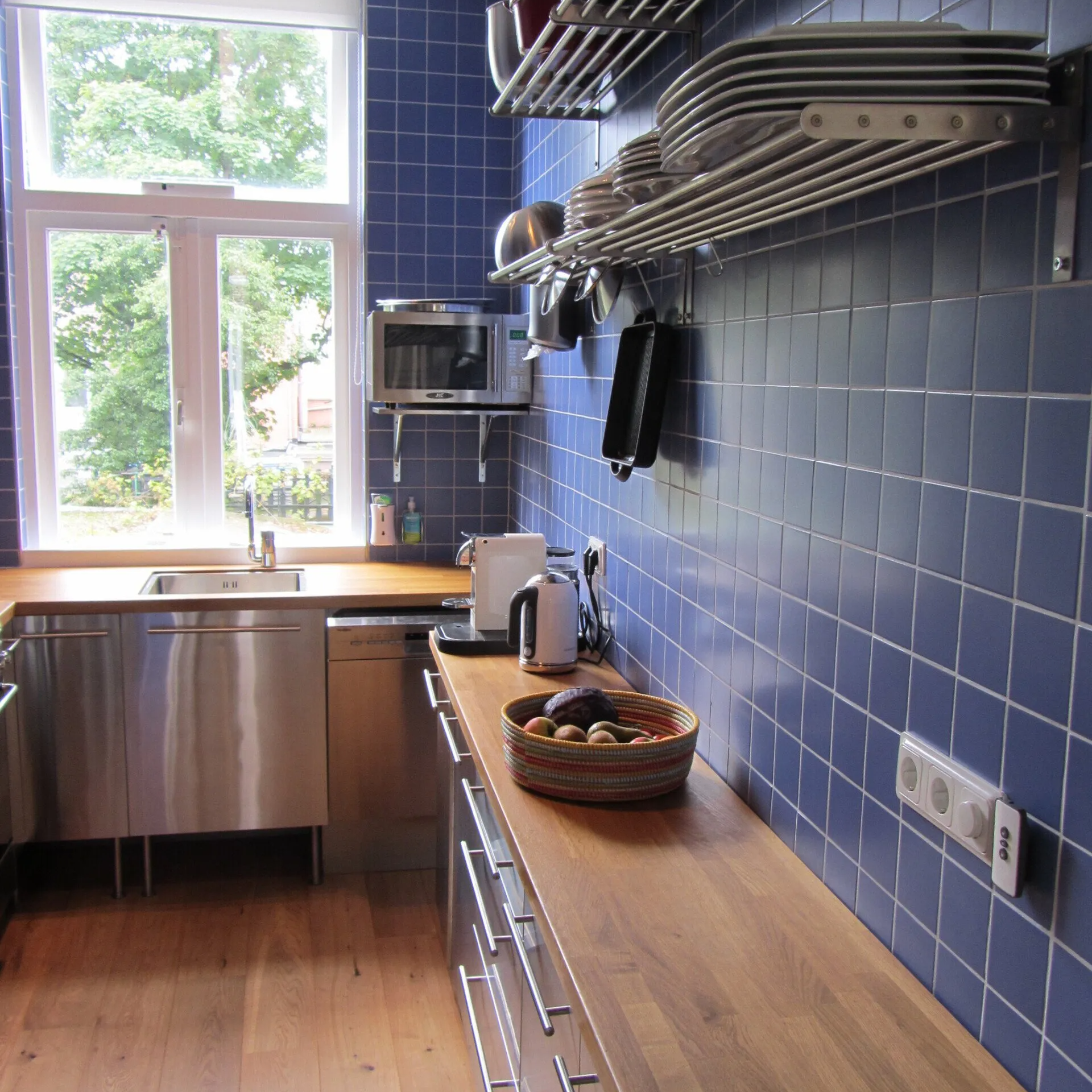 Een moderne keuken is voorzien van blauwe tegelwanden, houten aanrechtbladen, roestvrijstalen apparaten en aan de muur gemonteerde afwasrekken.