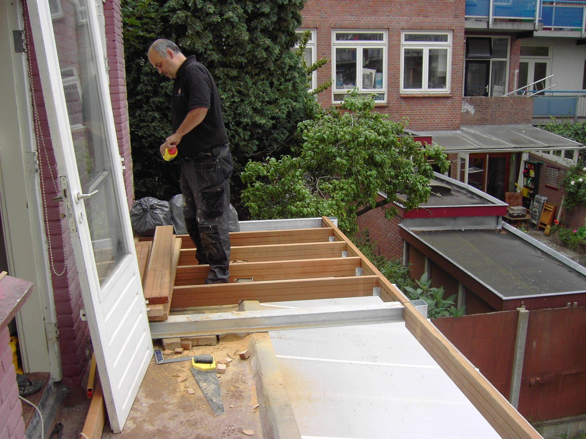 Een persoon staat op een houten platformconstructie in aanbouw, gezien vanaf een verhoogd standpunt.